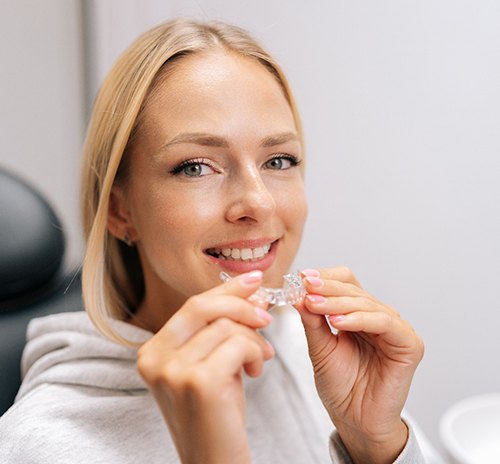 Closeup of woman smiling while holding clear aligner