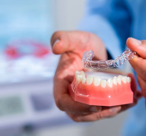 Dentist placing clear aligner on model of teeth