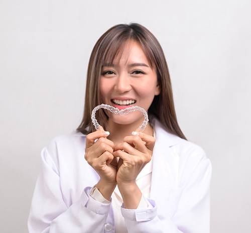 Woman smiling while creating heart-shape with clear aligners